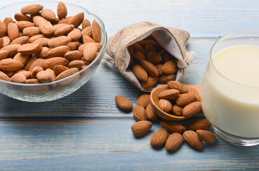 Close up view of healthy almond milk in drinking glass with seed in bowl on wooden background. Selective focus.