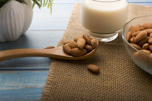 Close up view of healthy almond milk in drinking glass with seed in bowl on wooden background. Selective focus.