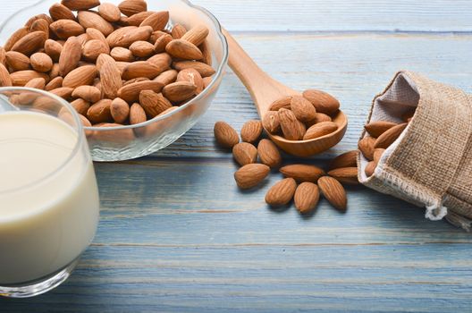 Close up view of healthy almond milk in drinking glass with seed in bowl on wooden background. Selective focus.