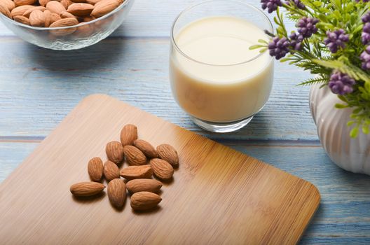 Close up view of healthy almond milk in drinking glass with seed in bowl on wooden background. Selective focus.