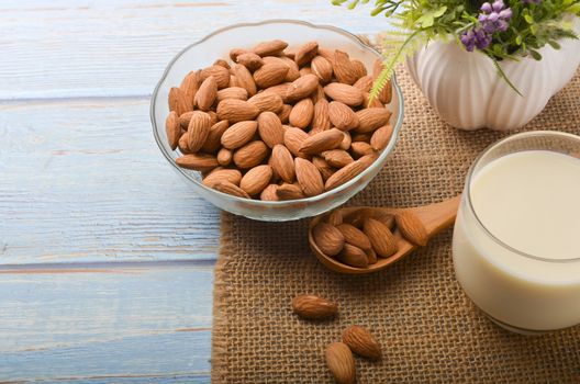 Close up view of healthy almond milk in drinking glass with seed in bowl on wooden background. Selective focus.