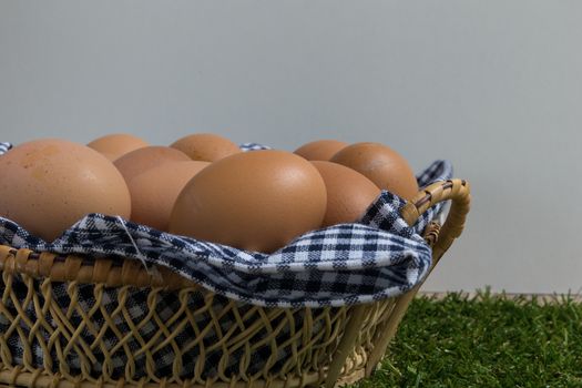 Basket contains group of chicken eggs put on grass.