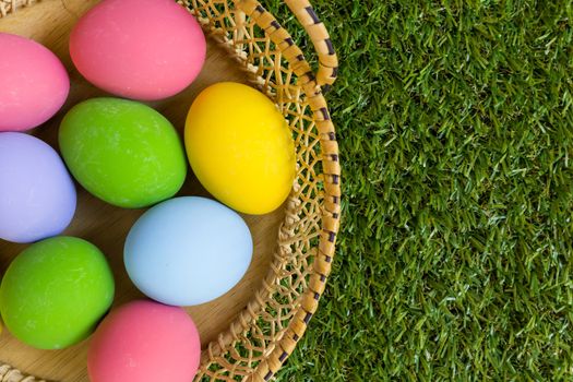 Group of colorful eggs in a basket placed on green grass field.