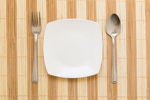 Empty plate with spoon and fork on table background.