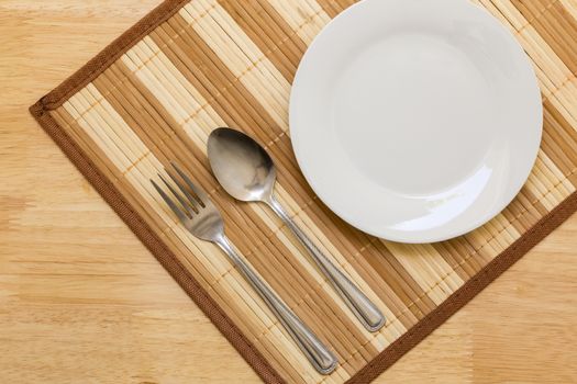 Empty plate with spoon and fork on table background.