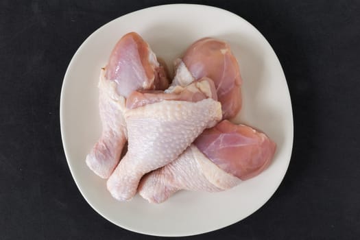 Fresh chicken legs on a plate on black background.