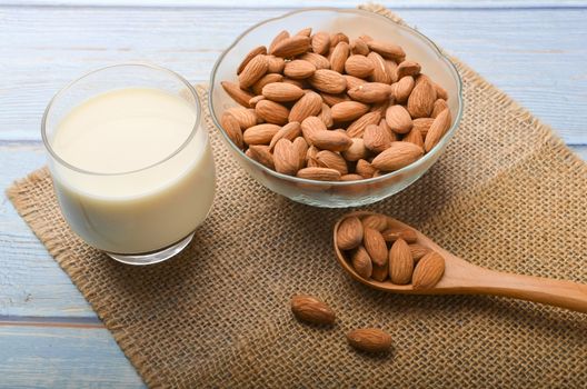 Close up view of healthy almond milk in drinking glass with seed in bowl on wooden background. Selective focus.