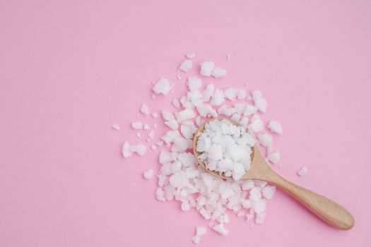 Sea salt in a wooden spoon on pink background for seasoning or preserving food