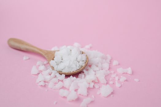 Sea salt in a wooden spoon on pink background for seasoning or preserving food