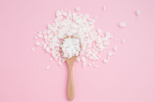 Sea salt in a wooden spoon on pink background for seasoning or preserving food