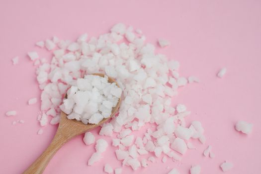 Sea salt in a wooden spoon on pink background for seasoning or preserving food