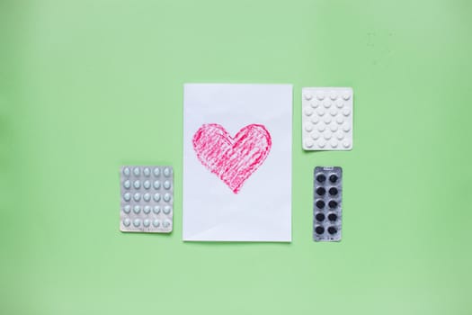 Greeting card with a painted red heart and pills. Medicine. Layout. Green background