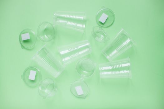 The layout on a green background from white plastic disposable cups. Caring for the environment. Recycling and sorting of garbage. Disposable tableware. Environmental pollution.
