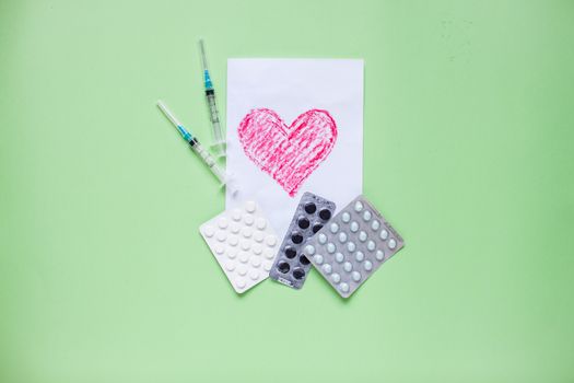 Greeting card with a painted red heart, blisters with pills, syringes. Medicine. Layout. Green background