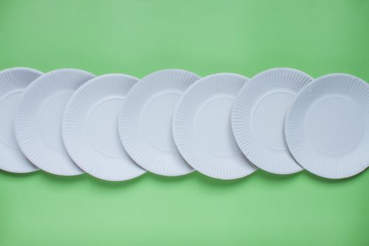 The layout on a green background from paper disposable plates. Caring for the environment. Recycling and sorting of garbage. Disposable tableware.