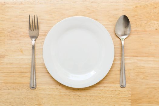 Empty plate with spoon and fork on table background.