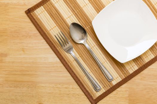 Empty plate with spoon and fork on table background.