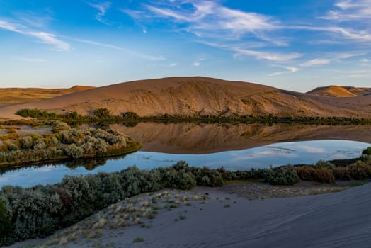 Desert oasis of water with vegetation along with blue sky and clouds at Bruneau Dunes, Idaho.