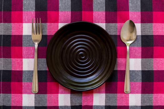 Empty plate with spoon and fork on table background.