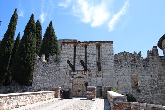 Stone wall with merlons and drawbridge gate of medieval castle of Brescia in north Italy