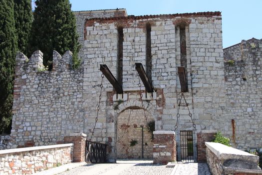 Stone wall with merlons and drawbridge gate of medieval castle of Brescia in north Italy