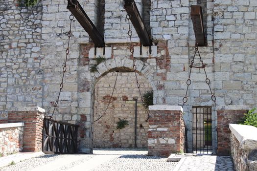 Stone wall with merlons and drawbridge gate of medieval castle of Brescia in north Italy