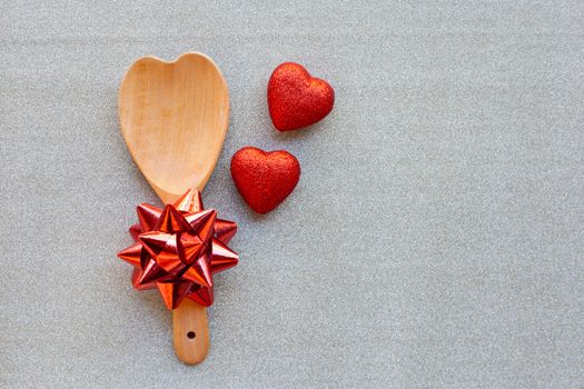 The red heart shapes and wooden spoon with red bow on silver glitter paper background in love concept for valentines day.