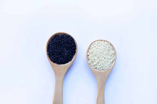 Black and white sesame seeds on wooden spoon, white background. Copy space