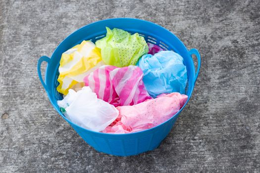 Colorful plastic bags in trash basket on cement floor background.