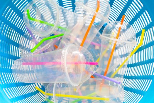 Plastic cups with straws in waste basket.