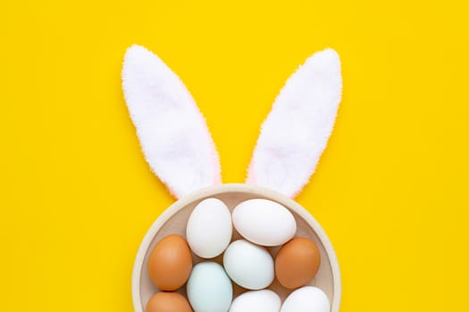 Top view of cute bunny ears with eggs on yellow background. Easter concept