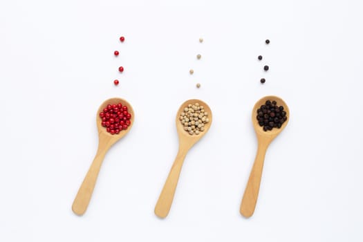 Red, white and black peppercorns with wooden spoon on white background.