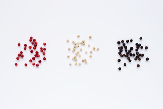 Red, white and black peppercorns on white background.