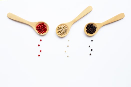 Red, white and black peppercorns with wooden spoon on white background.