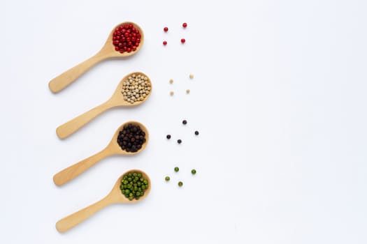 Green, red, white and black peppercorns with wooden spoon on white background.