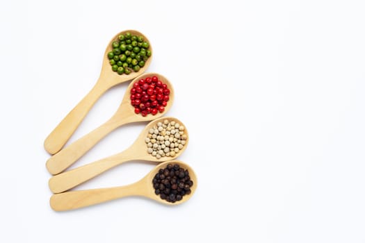 Green, red white and black peppercorns with wooden spoon on white background.