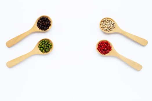 Red, green, white and black peppercorns with wooden spoon on white background.