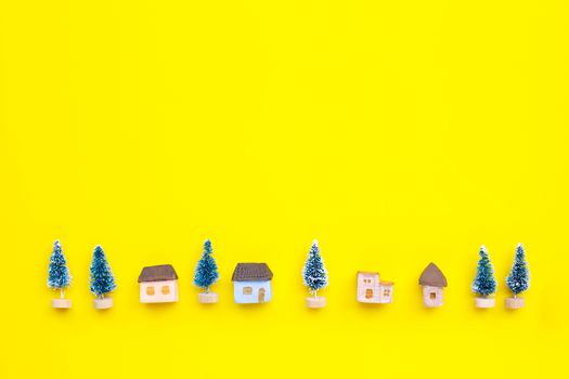 Merry Christmas and Happy Holidays, Miniature house with fir trees on yellow background. Copy space