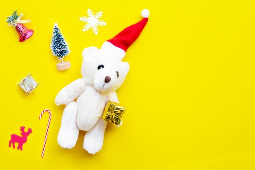 Christmas composition, Toy bear wearing a santa hat with  gifts, pine tree and decorations on yellow background. Copy space, Christmas holidays concept