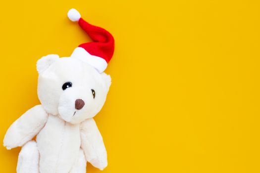 Toy bear wearing a santa hat on yellow background. Christmas holidays concept