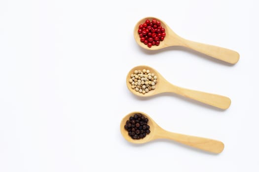Red, white and black peppercorns with wooden spoon on white background.