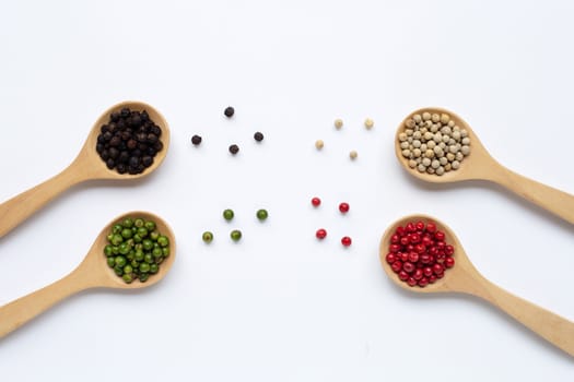 Green, red, white and black peppercorns with wooden spoon on white background.
