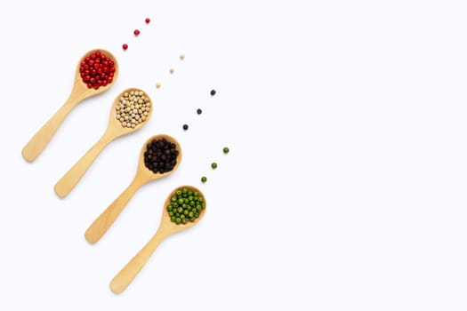 Green, red white and black peppercorns with wooden spoon on white background.