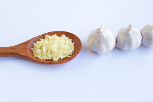Fresh chopped garlic  on wooden spoon with garlic head on white background.