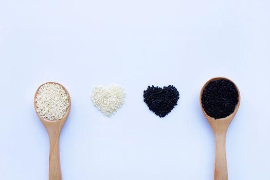 Black and white sesame seeds on wooden spoon, white background. 