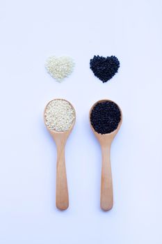 Black and white sesame seeds on wooden spoon, white background. Copy space