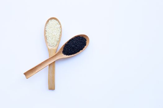 Black and white sesame seeds on wooden spoon, white background. Copy space