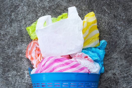 Colorful plastic bags with trash basket on cement floor background.