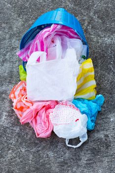 Colorful plastic bags with trash basket on cement floor background.