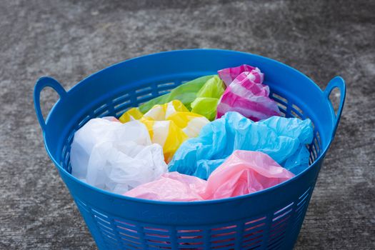 Colorful plastic bags in blue waste basket on cement floor background.